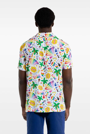 A man is wearing a white Hawaiian shirt with a rainbow pride print, Print consists of peace symbols, hearts and other icons, Also, wearing blue pants. He is facing away from the camera and showing the back side of the shirt.
