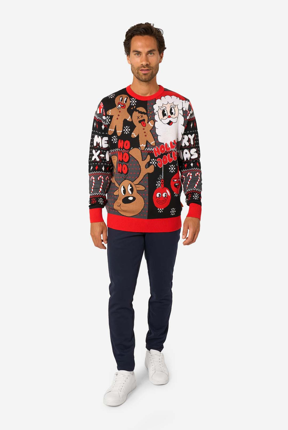 A man modeling a black Christmas crewneck sweater with colorful holiday graphics including gingerbread men, Santa, a reindeer, and 'Holly, No, Holly' text, paired with navy pants against a light gray studio background.