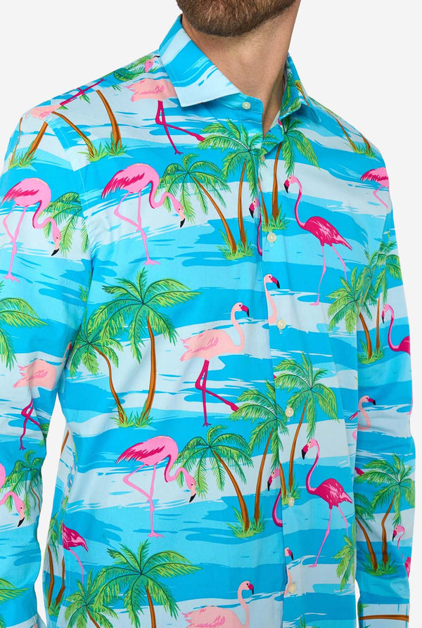 Man wearing a Shirt with flamingos and palm tree pattern on a blue background, chest close up.