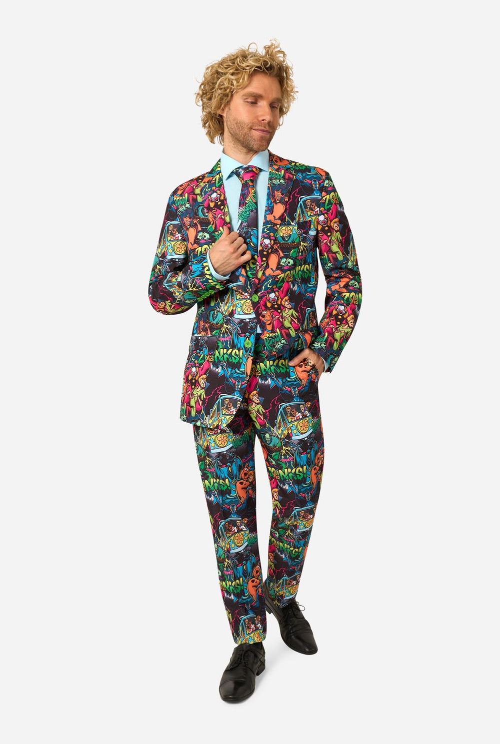 A man with curly blond hair wearing a vibrant, multicolored Scooby-Doo-patterned suit, a light blue dress shirt, and a matching tie, standing against a solid light gray background.