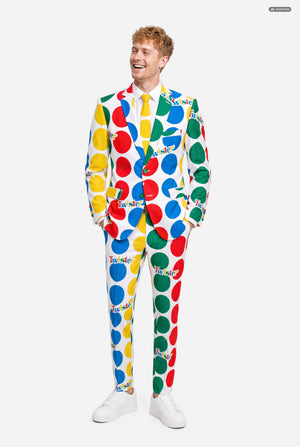A man wearing a white suit with large multicolored polka dots and the Twister logo, resembling a Twister mat paired with a white and yellow tie, against a light gray studio background. Full body image