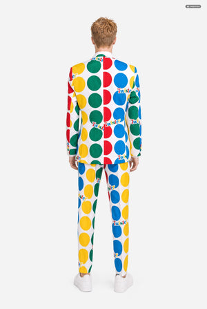 A man wearing a white suit with large multicolored polka dots and the Twister logo, resembling a Twister mat paired with a white and yellow tie, against a light gray studio background. View from the back.
