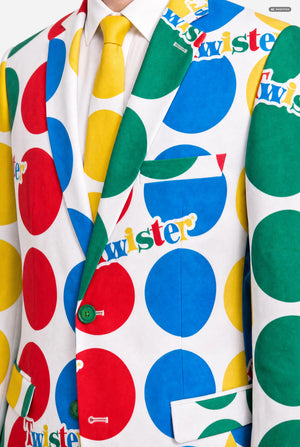 A man wearing a white suit with large multicolored polka dots and the Twister logo, resembling a Twister mat, against a light gray studio background. Chest close-up.