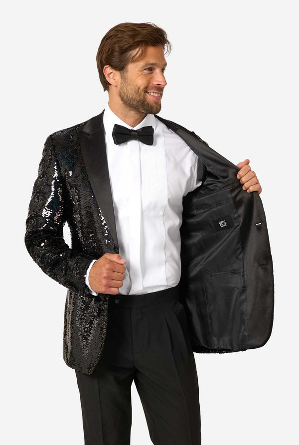 Man wearing a black sequin tuxedo jacket over a white shirt with a bow tie on a white background