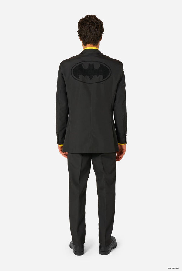 Person wearing a black suit with a Batman logo on the back, standing against a white background. View from the back