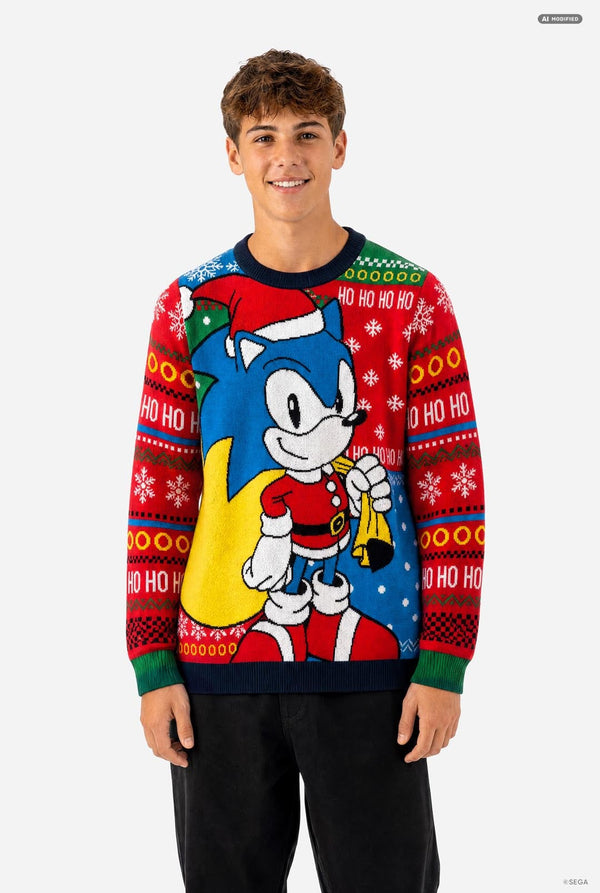 A young man wearing a festive red and blue Christmas crewneck sweater featuring Sonic the Hedgehog, standing against a plain light gray background.