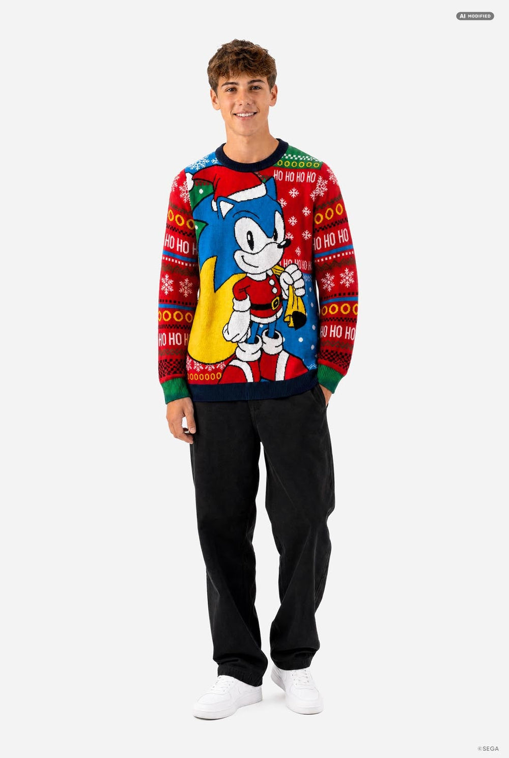 A young man wearing a festive red and blue Christmas crewneck sweater featuring Sonic the Hedgehog, standing against a plain light gray background.