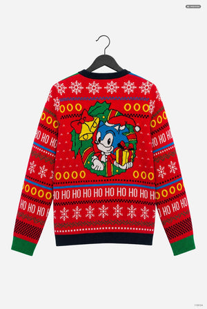 A red Christmas sweater featuring Sonic the Hedgehog, hanging on a black hanger against a light gray background. The sweater has a festive pattern with snowflakes, 'HO HO HO' text, and a central graphic of Sonic wearing a Santa hat and holding a gift.