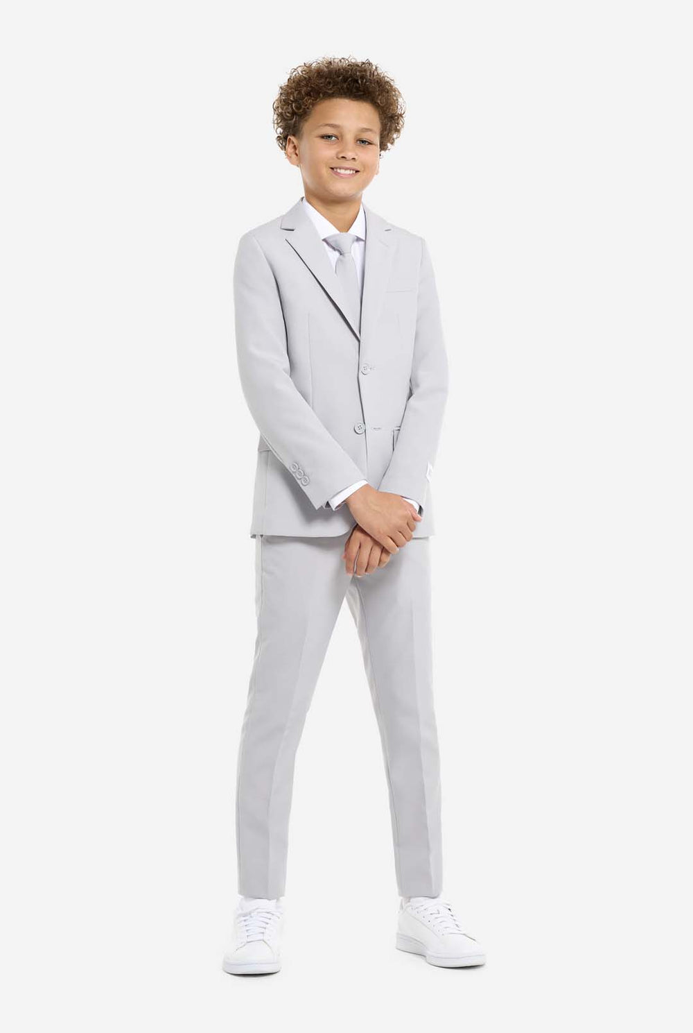 In this image, a kid is wearing a formal grey suit. The suit consists of a blazer, pants and tie. Kid has one hand in pocket.