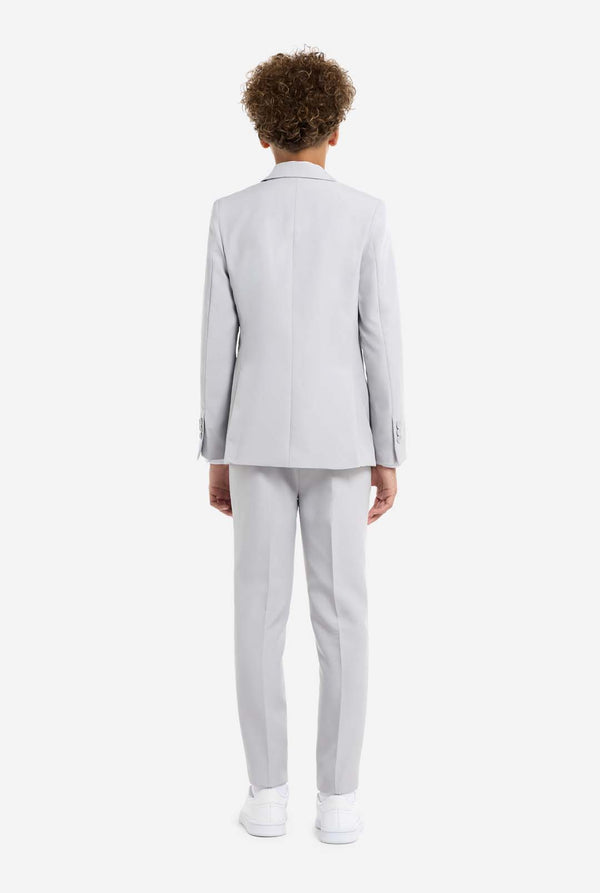 In this image, a kid is wearing a formal grey suit. The suit consists of a blazer, pants and tie. View from the back.