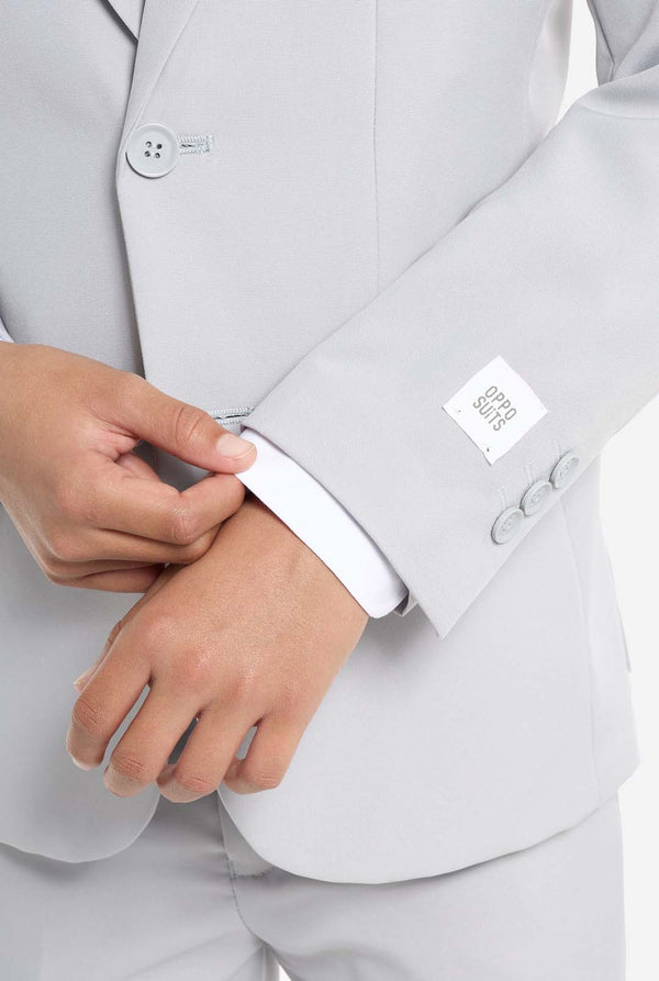 In this image, a kid is wearing a formal grey suit. The suit consists of a blazer, pants and tie. Sleeve close up.