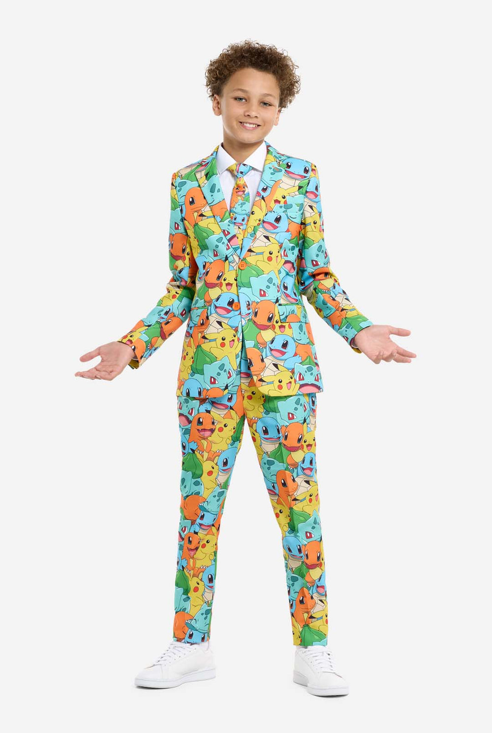 Teen wearing formal multi color suit with all-over Pokemon print. The suit contains the characters Pikachu, Bulbasaur, Charmander and Squirtle. Kid stands with hands in pockets.