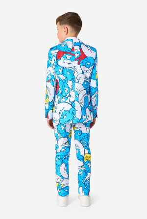 Teen boy wearing a vibrant Smurfs kids suit with colorful cartoon character prints in blue, red, yellow, and white, paired with a matching tie and white shirt, smiling against a plain background. View from the back.