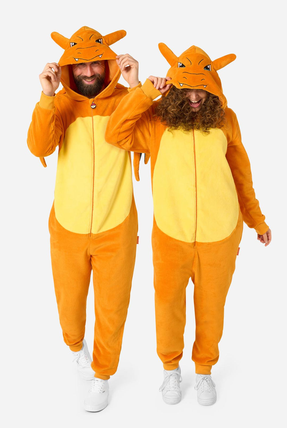 Two people wearing matching orange and yellow Charizard-themed hooded onesies against a plain light gray background.