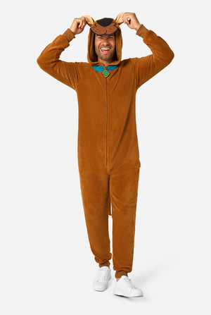 A man wearing a brown full-body Scooby-Doo onesie costume with white sneakers, holding the hood up with both hands against a light gray studio background.