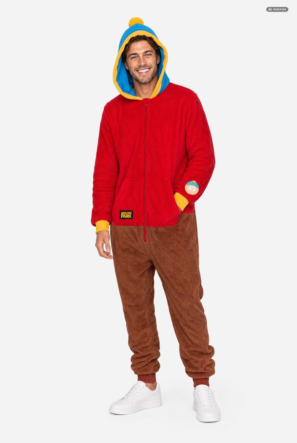 A man wearing a South Park Stan Onesie, red and brown hooded zip-up onesie pajama with a blue and yellow hood, yellow cuffs, a South Park patch on the sleeve, and brown pants, photographed against a light gray studio background.