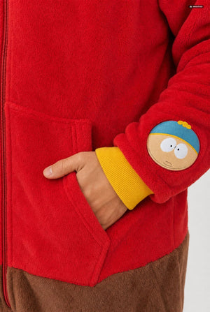 A man wearing a South Park Stan Onesie, red and brown hooded zip-up onesie pajama with a blue and yellow hood, yellow cuffs, a South Park patch on the sleeve, and brown pants, photographed against a light gray studio background. Sleeve close up.