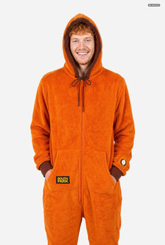 A smiling man wearing an orange South Park Kenny onesie with brown drawstrings and cuffs, standing against a light gray background. A small patch on the left leg reads 'South Park'.  