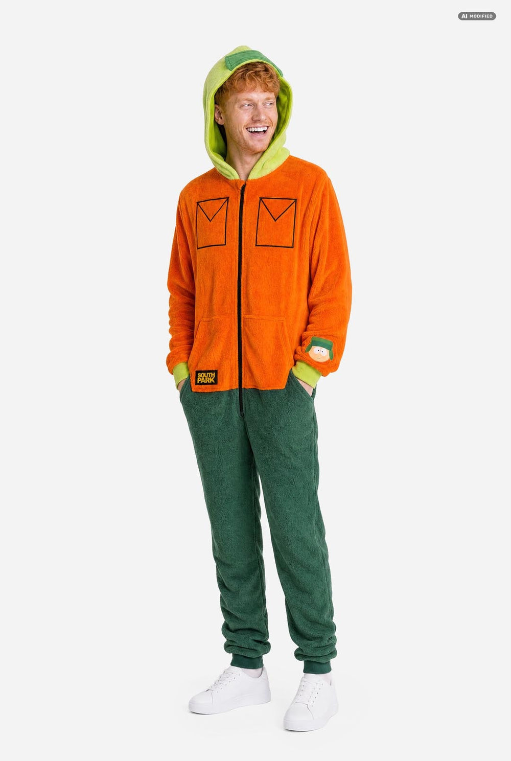 A man wearing a bright orange South Park Kyle onesie costume with lime green hood lining and cuffs, plus dark green pants, photographed against a light gray studio background.