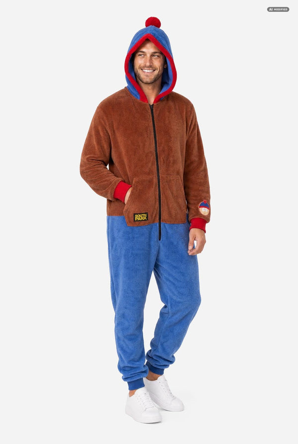 A man wearing a brown and blue South Park Stan onesie with blue and red hood lining, and a South Park patch on the sleeve, photographed against a light gray studio background. Full body image