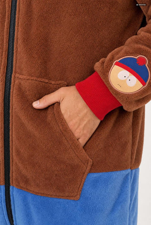Close-up of a brown fleece zip-up jacket with a red ribbed cuff featuring a South Park character patch, and a blue lower section, shown on a person with a hand in the pocket.