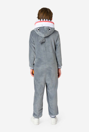A child shown from the back wearing a gray shark-themed hooded one-piece onesie with white and red details around the hood, standing against a plain light gray background.