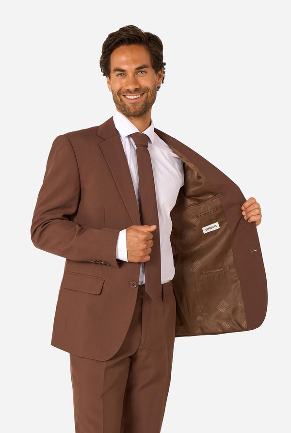Man wearing a brown suit with a white shirt and tie, holding the jacket open.