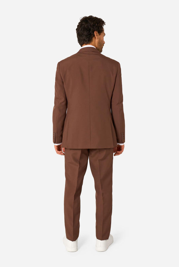 Man wearing a brown suit standing against a white background. View from the back