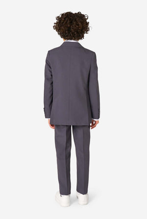 A child model shown from the back wearing a dark gray two-piece suit with white sneakers, photographed against a clean white studio background.