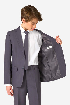Young boy wearing a gray suit with a white shirt and tie, holding open his jacket to reveal a brand label.