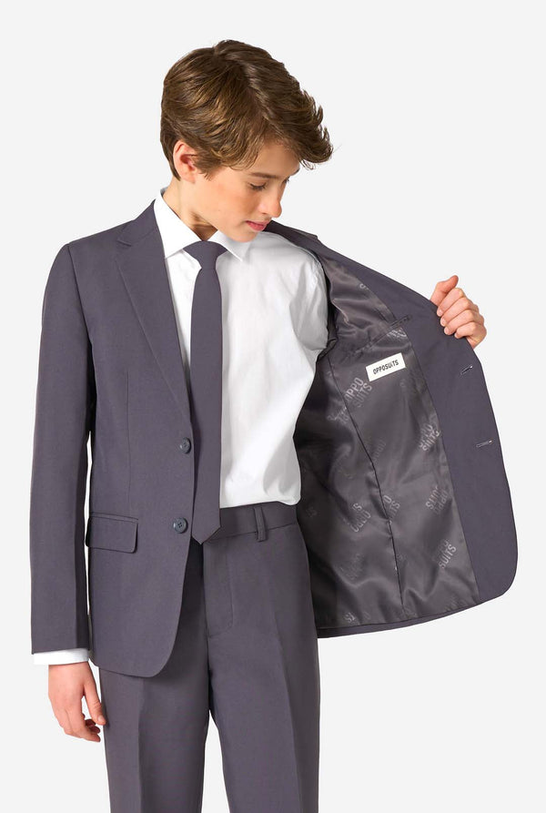 Young boy wearing a gray suit with a white shirt and tie, holding open his jacket to reveal a brand label.