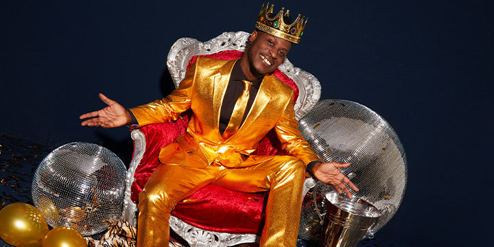 Man on chair in golden suit, with discoballs besides the chair.