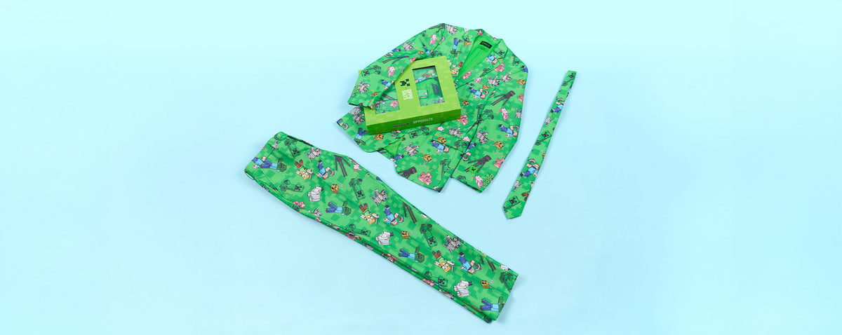 A green patterned, Minecraft themed fabric clothing set laid flat on a light blue background, including a long rectangular piece, a smaller matching strip, and a folded top with a green rectangular accessory placed on top.