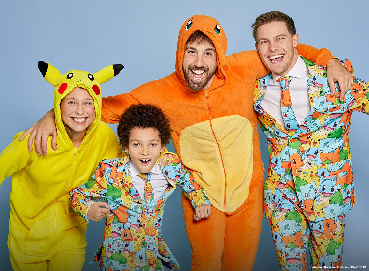 Four people posing together in colorful Pokémon-themed onesies and suits against a light blue studio background. The group includes a woman in a yellow Pikachu onesie, a man in an orange Charizard onesie, a man in a multicolor Squirtle suit, and a young boy in a matching multicolor onesie.