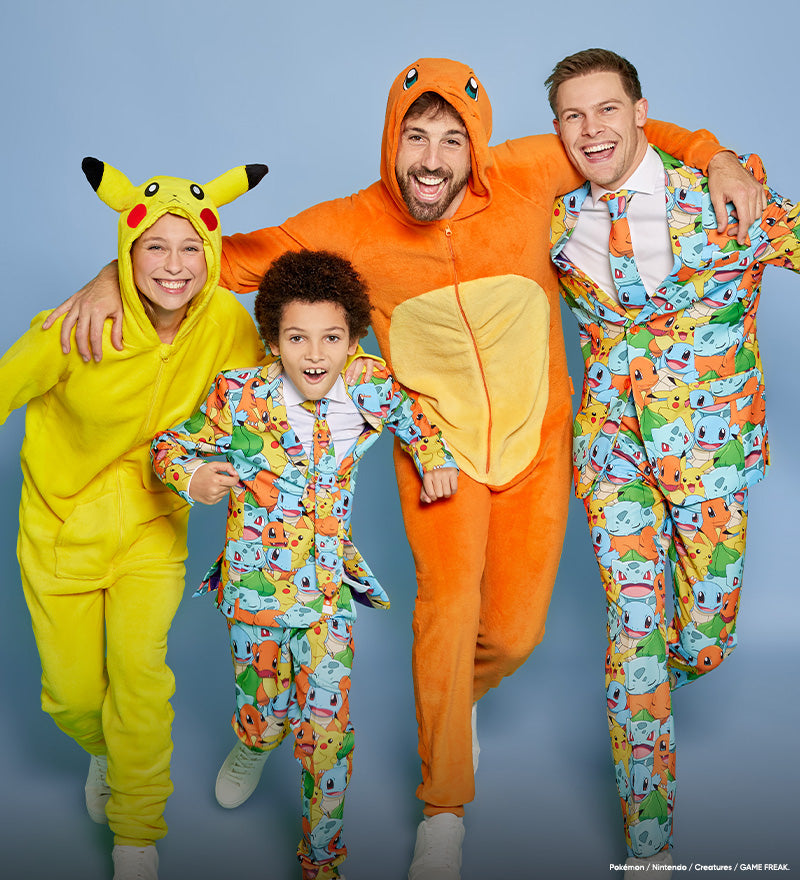 Four people posing together in colorful Pokémon-themed onesies and suits against a light blue studio background. The group includes a woman in a yellow Pikachu onesie, a man in an orange Charizard onesie, a man in a multicolor Squirtle suit, and a young boy in a matching multicolor onesie.