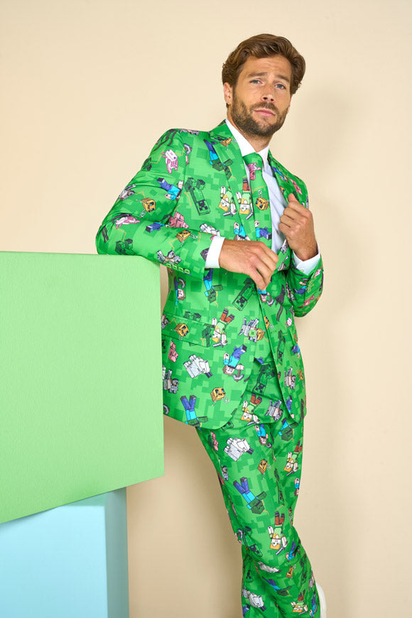 Man wearing a green patterned suit against a beige background, leaning against a stack of blocks
