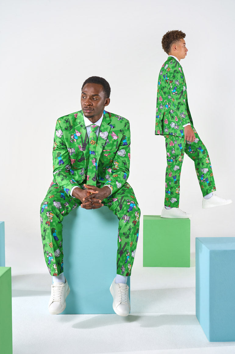 Two men wearing green Minecraft suits sitting and standing on  blocks that are laying on the ground.