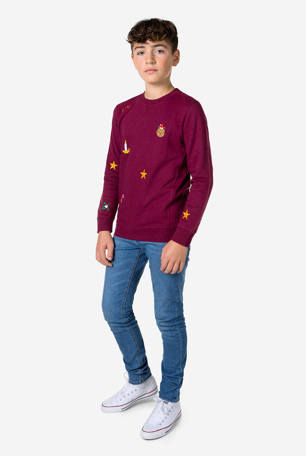 Teen wearing burgundy red Christmas sweater with colored Christmas icons and blue jeans